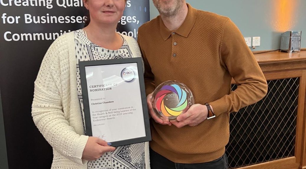 Christine standing with a man holding her award in front of an OCN banner
