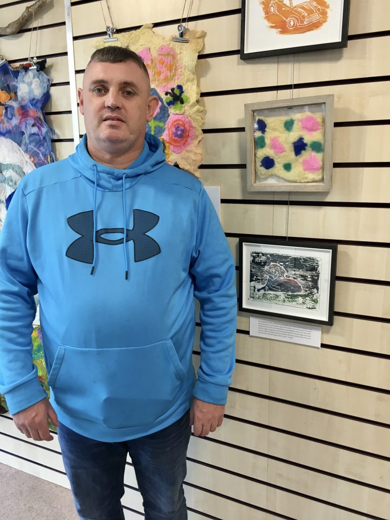 Francis, a participant, standing beside his artwork on display