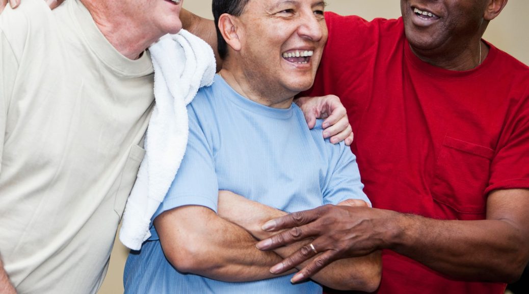 Three men aged around 60 smiling and laughing with their arms round each other.