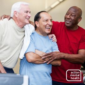 Three men aged around 60 smiling and laughing with their arms round each other.
