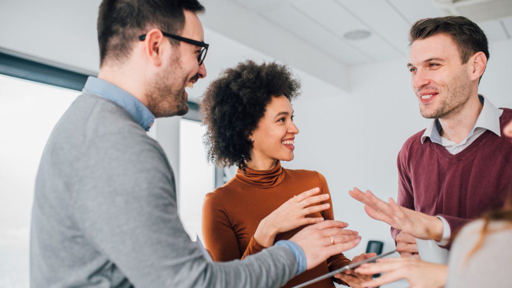 Three colleagues chatting and smiling in an office. 