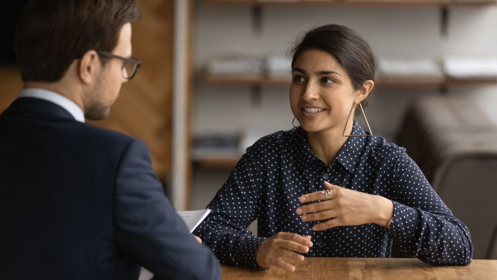 Two colleagues having a conversation at a desk. 