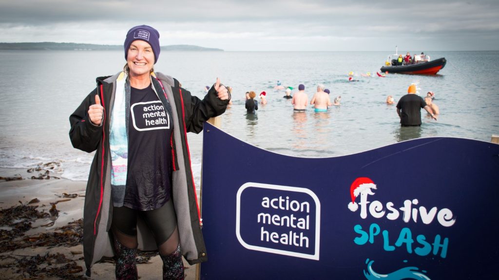 A Festive Splash participant on the beach. She is smiling and wearing an Action Mental Health t-shirt.