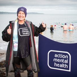 A Festive Splash participant on the beach. She is smiling and wearing an Action Mental Health t-shirt.