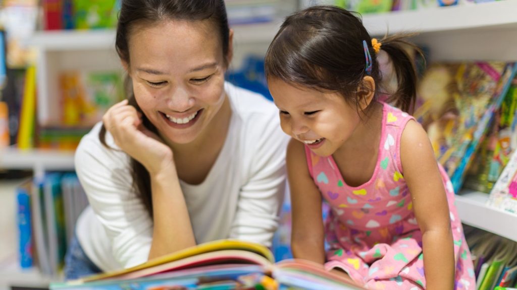 A mother and young daughter reading a children's book in a library.