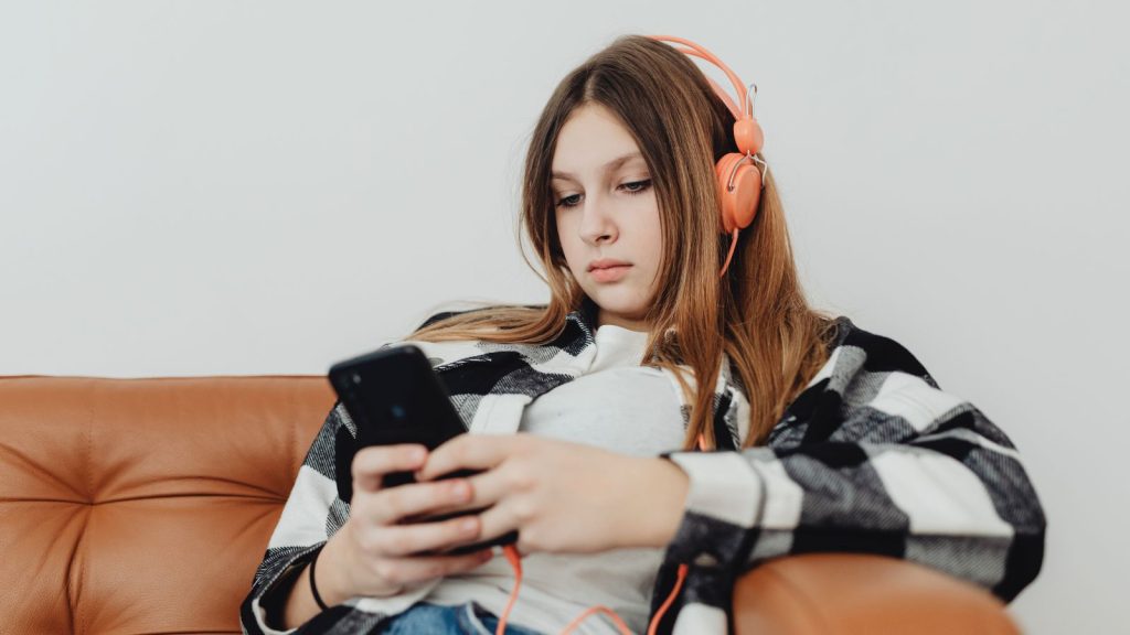 A teenage girl wearing headphones and scrolling on her phone.