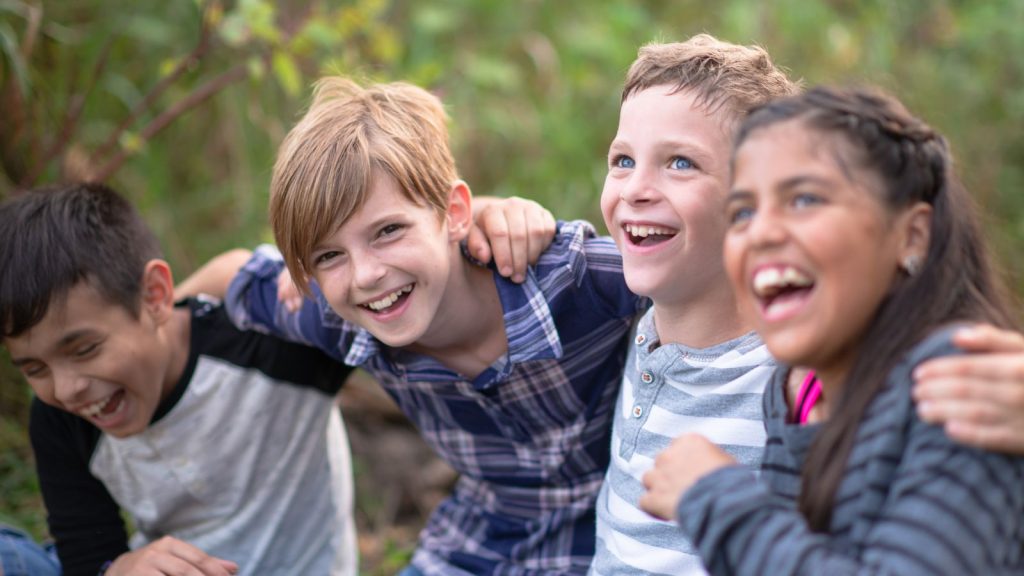 A group of 4 children laughing and smiling while sitting in a park.