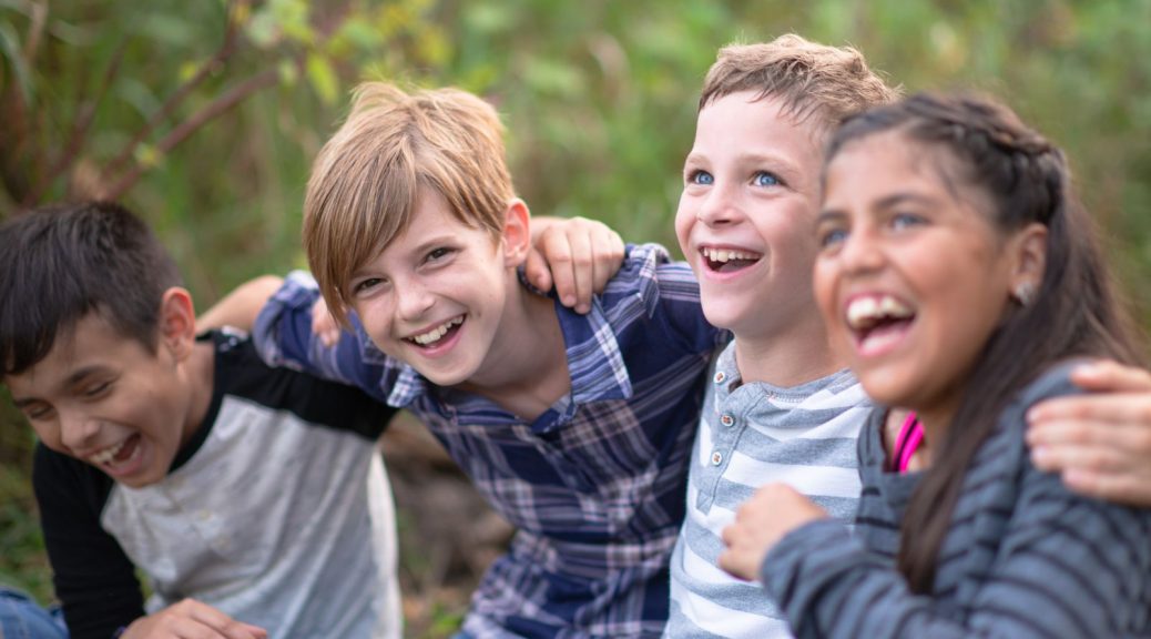 A group of 4 children laughing and smiling while sitting in a park.