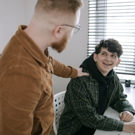 A man stands with his hand on another young man's shoulder in a show of support.