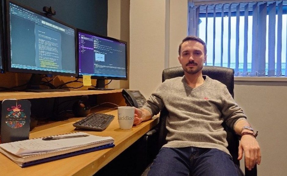 Illya sits at his work desk in front of his computer.