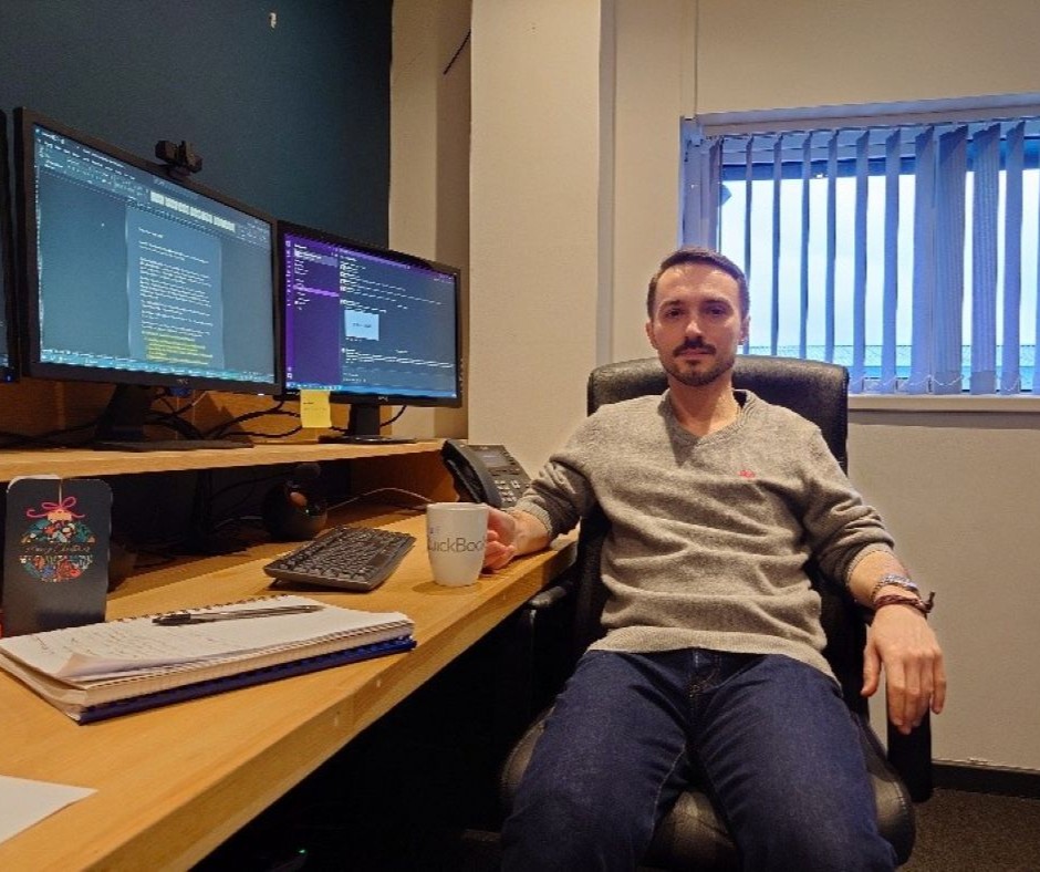 Illya sits at his work desk in front of his computer.