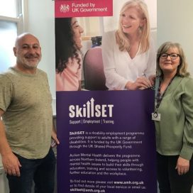 Client in our Lisburn service standing beside a SkillSET banner and a member of staff from Action Mental Health.