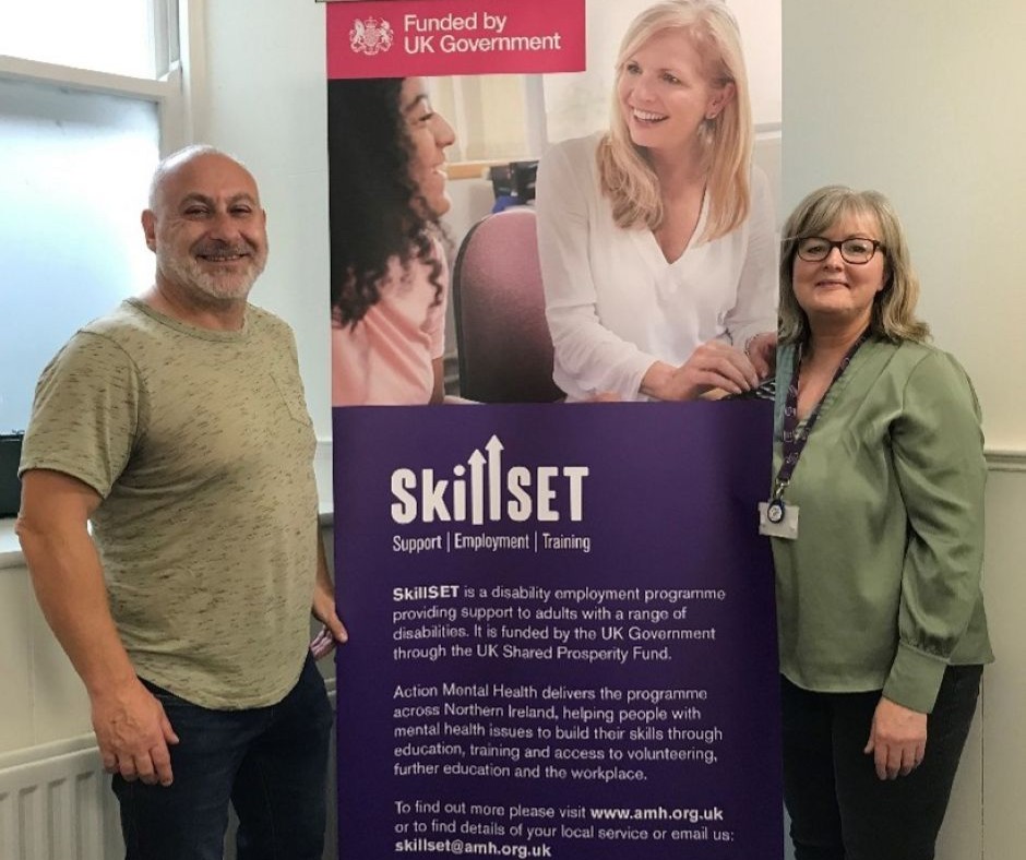 Client in our Lisburn service standing beside a SkillSET banner and a member of staff from Action Mental Health.