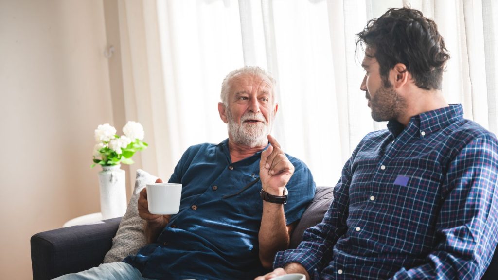 An older father having a cup of tea and talking to his adult son.