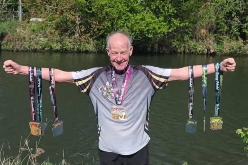 Eugene stands with arms outstretched, holding 6 marathon medals.