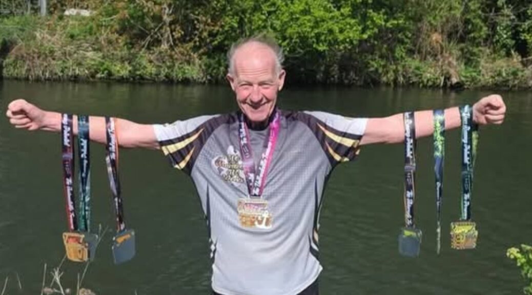 Eugene stands with arms outstretched, holding 6 marathon medals.