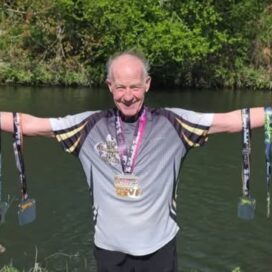 Eugene stands with arms outstretched, holding 6 marathon medals.