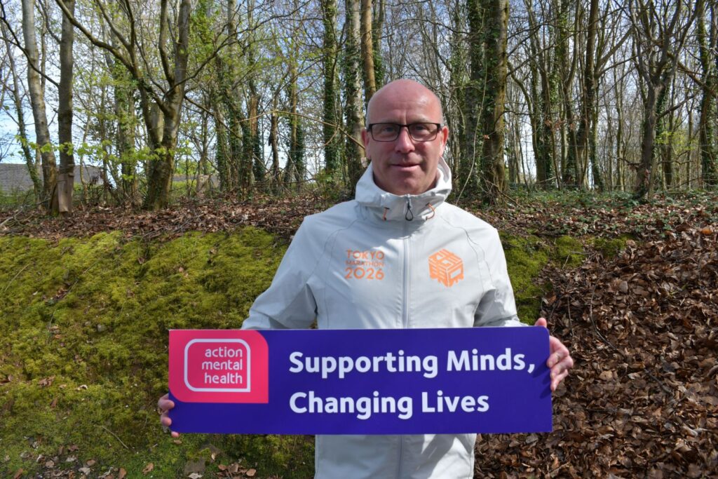 Stuart wearing a Tokyo Marathon 2026 running jacket and holding a sign for Action Mental Health.