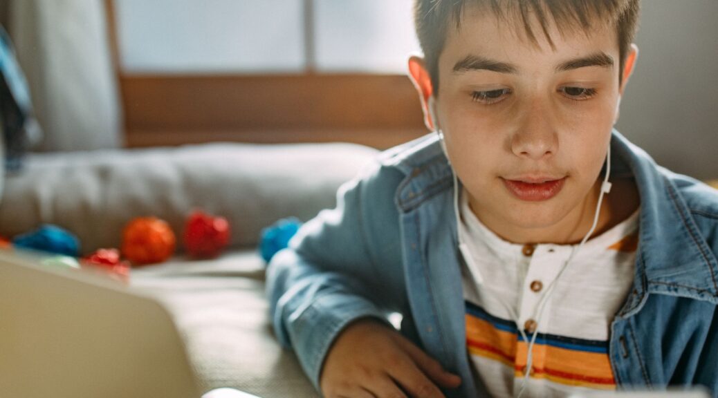 A teenage boy scrolling on his phone while sitting by a laptop,