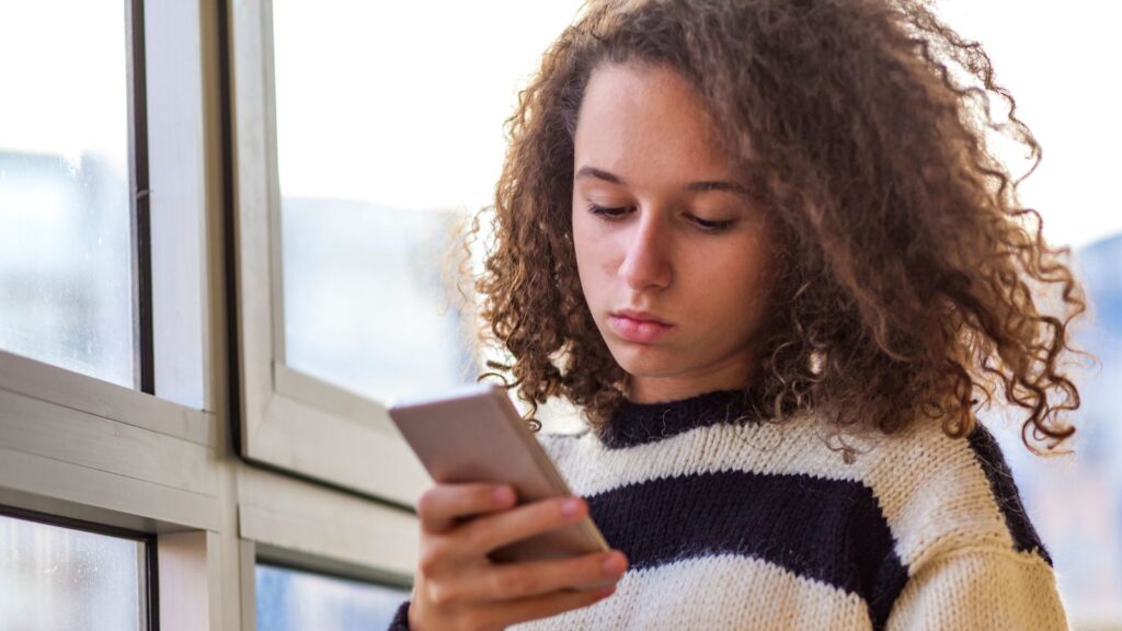 A teenage girl scrolling on her phone, looking serious.