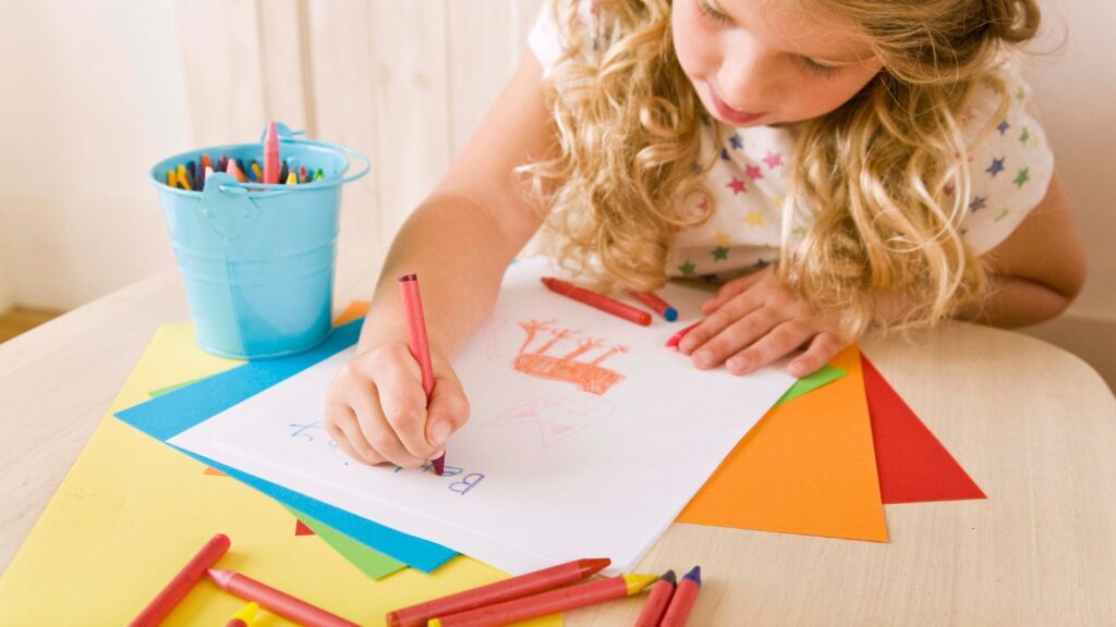 A girl drawing a picture with crayons.