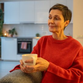 A middle-aged woman sitting on a sofa, peacefully drinking tea.