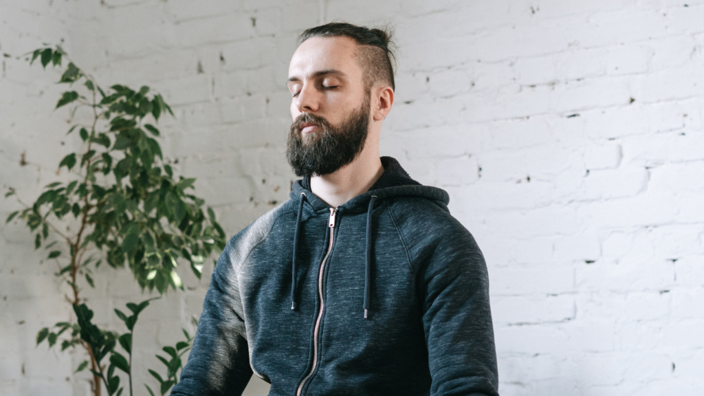 A man in his 30s sitting with his eyes closed, breathing mindfully.