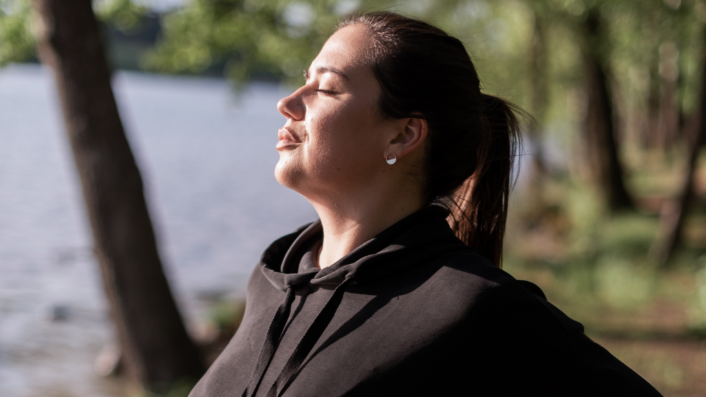 A young woman standing outside, enjoying fresh air and sunshine on her face.