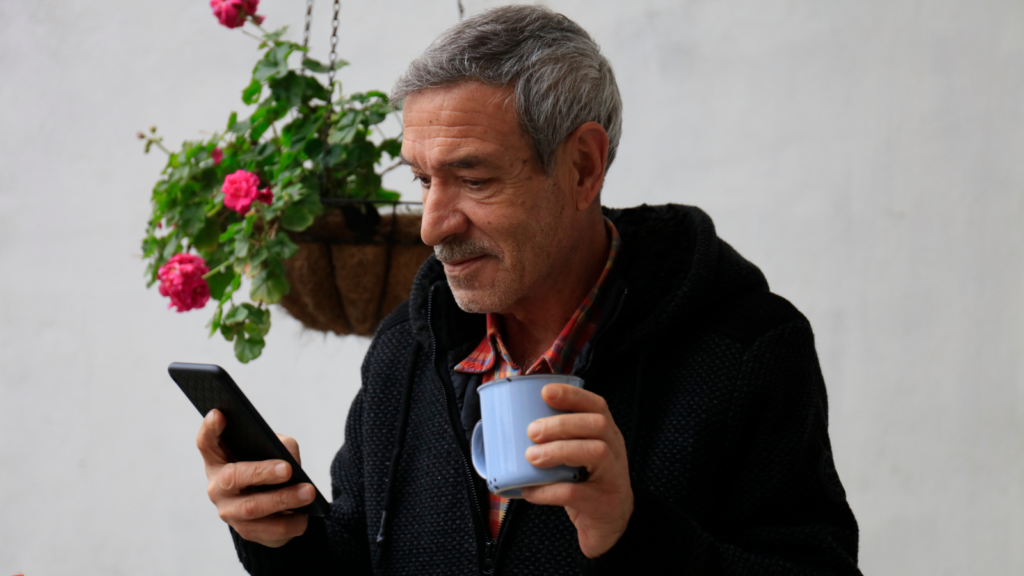 An older man typing on his phone, looking relaxed.