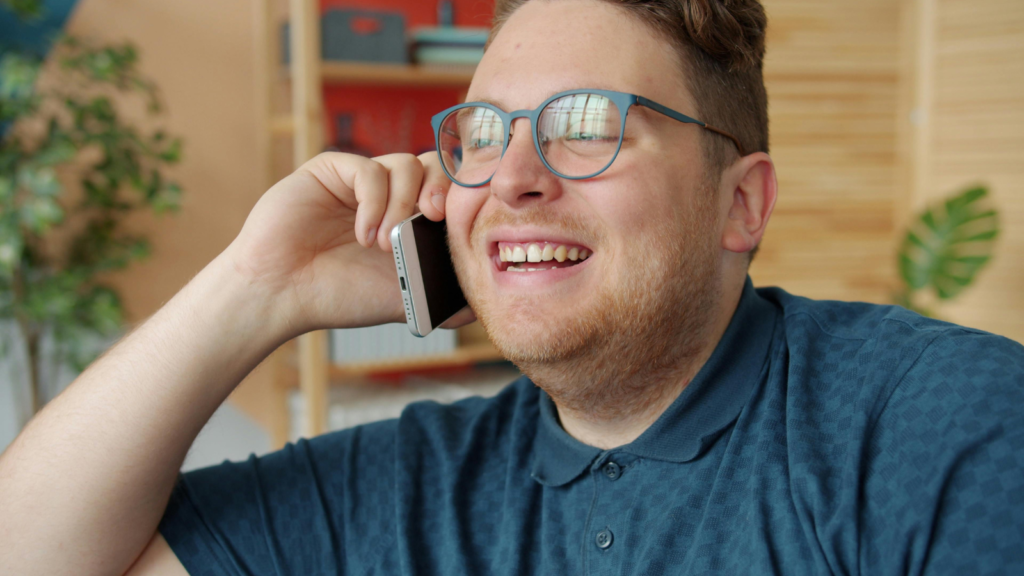 A young man smiling while chatting on the phone.