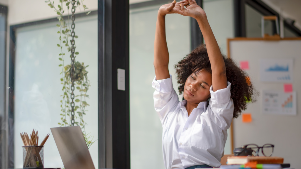 A young professional woman stretching at her desk.
